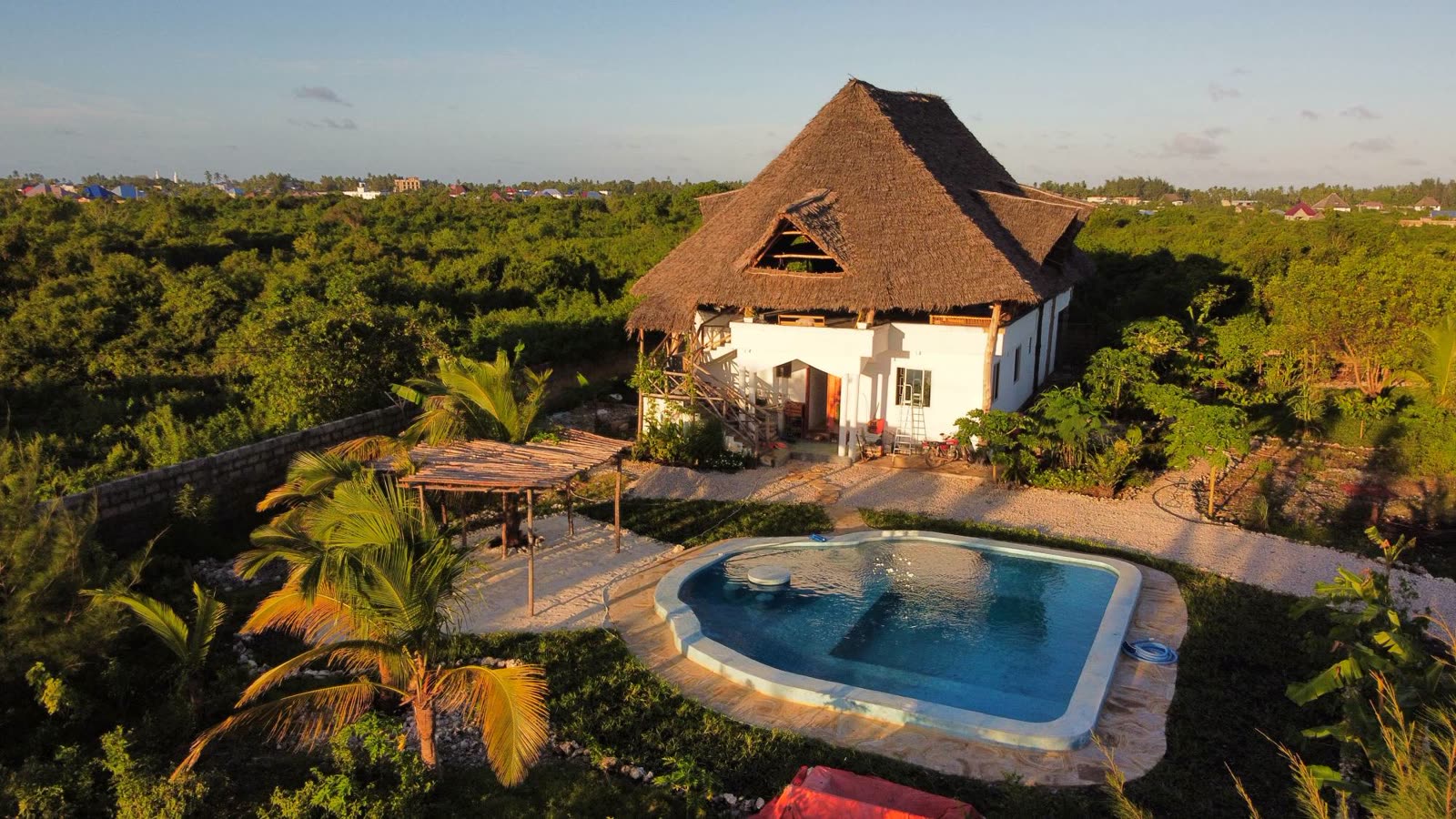 TideTribe in Paje auf Sansibar: Haus mit Strohdach, Pool und Palmen im Abendlicht